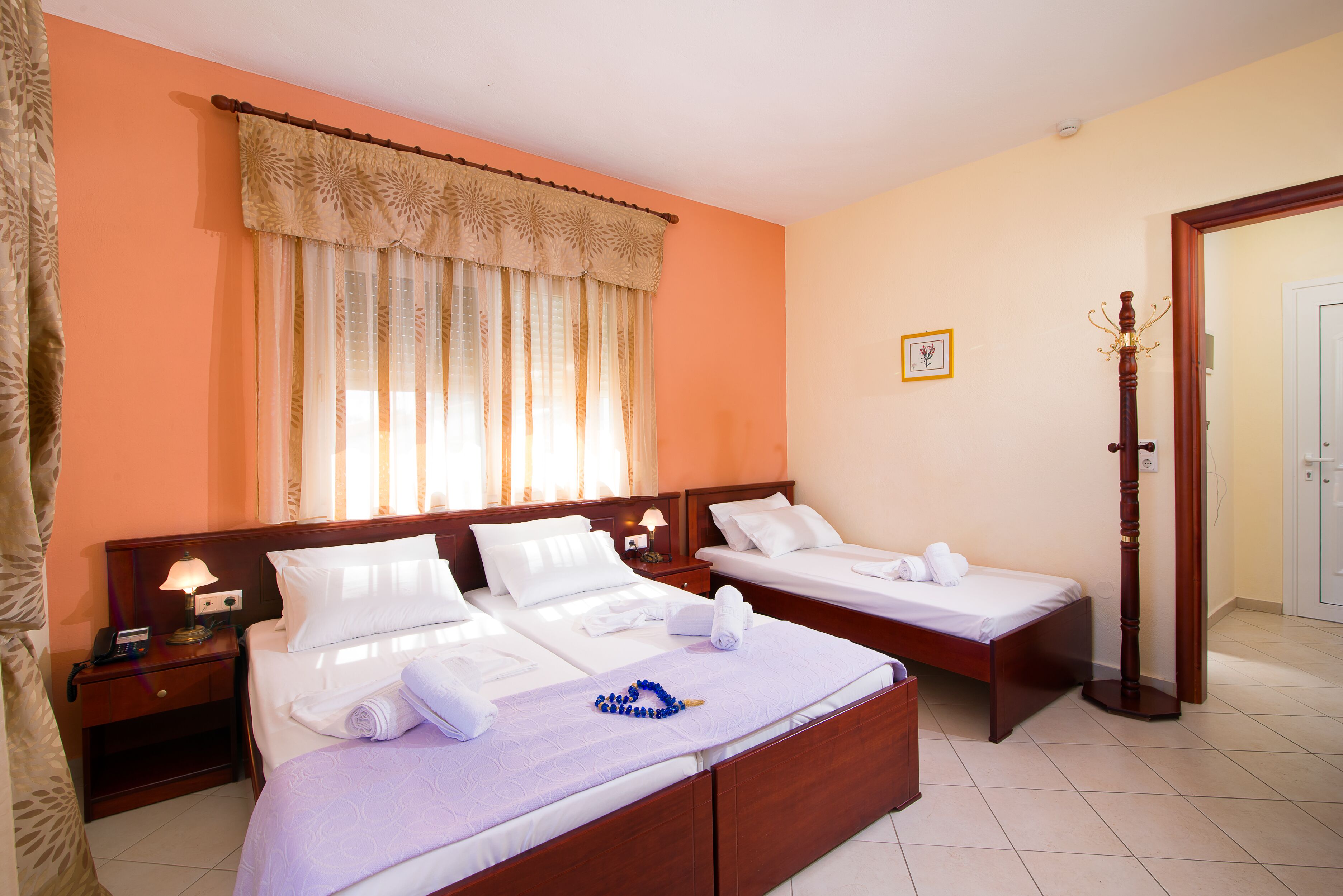 A hotel room with two beds, a nightstand with a lamp, a wooden floor, and a window with curtains.