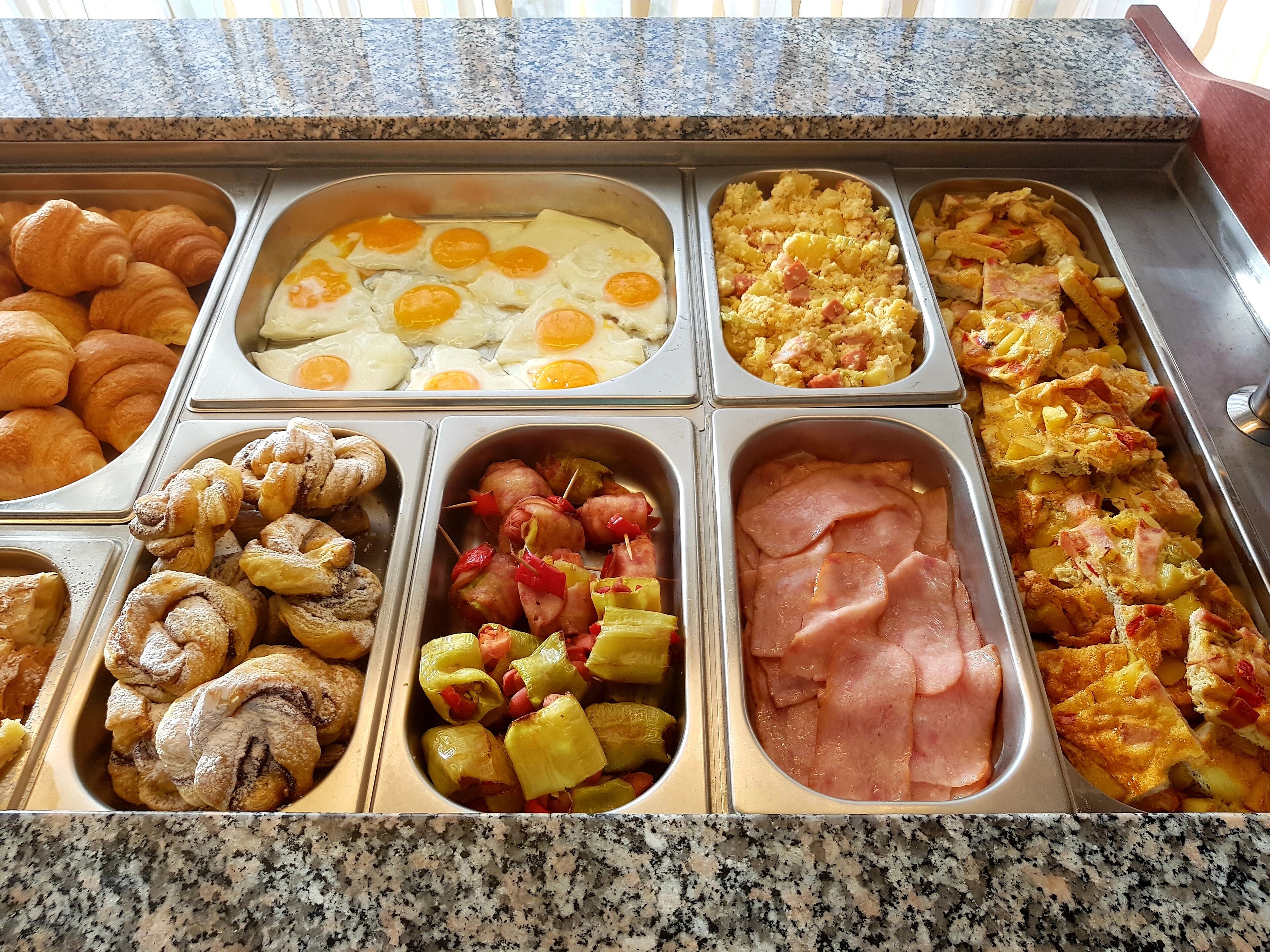 Un bufé con diversos alimentos, como huevos, jamón y pastelería.