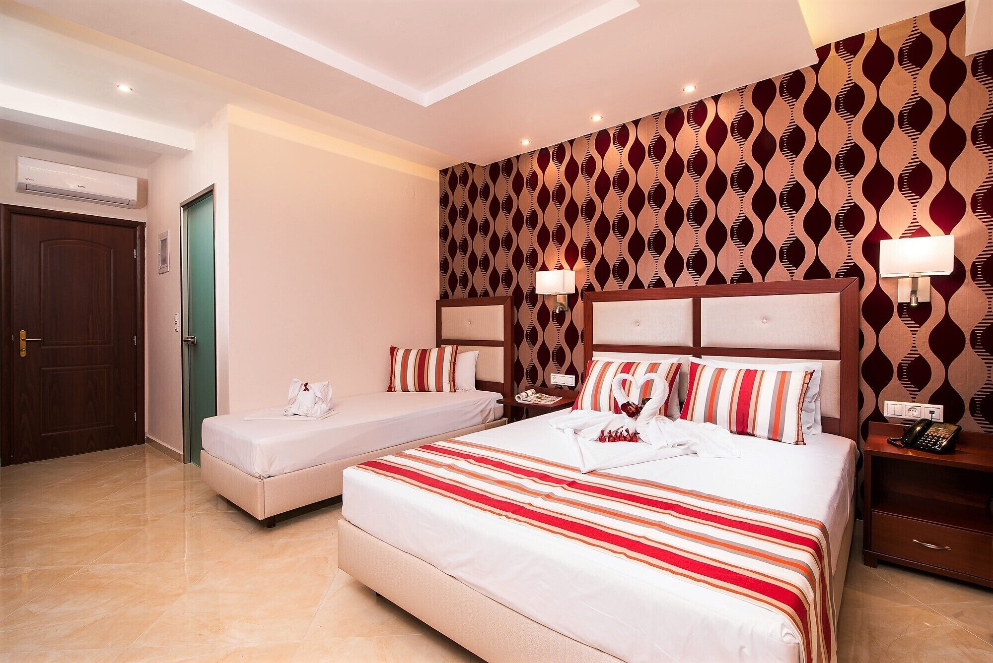 A hotel room with two beds, a minibar, a desk, and a patterned wall.