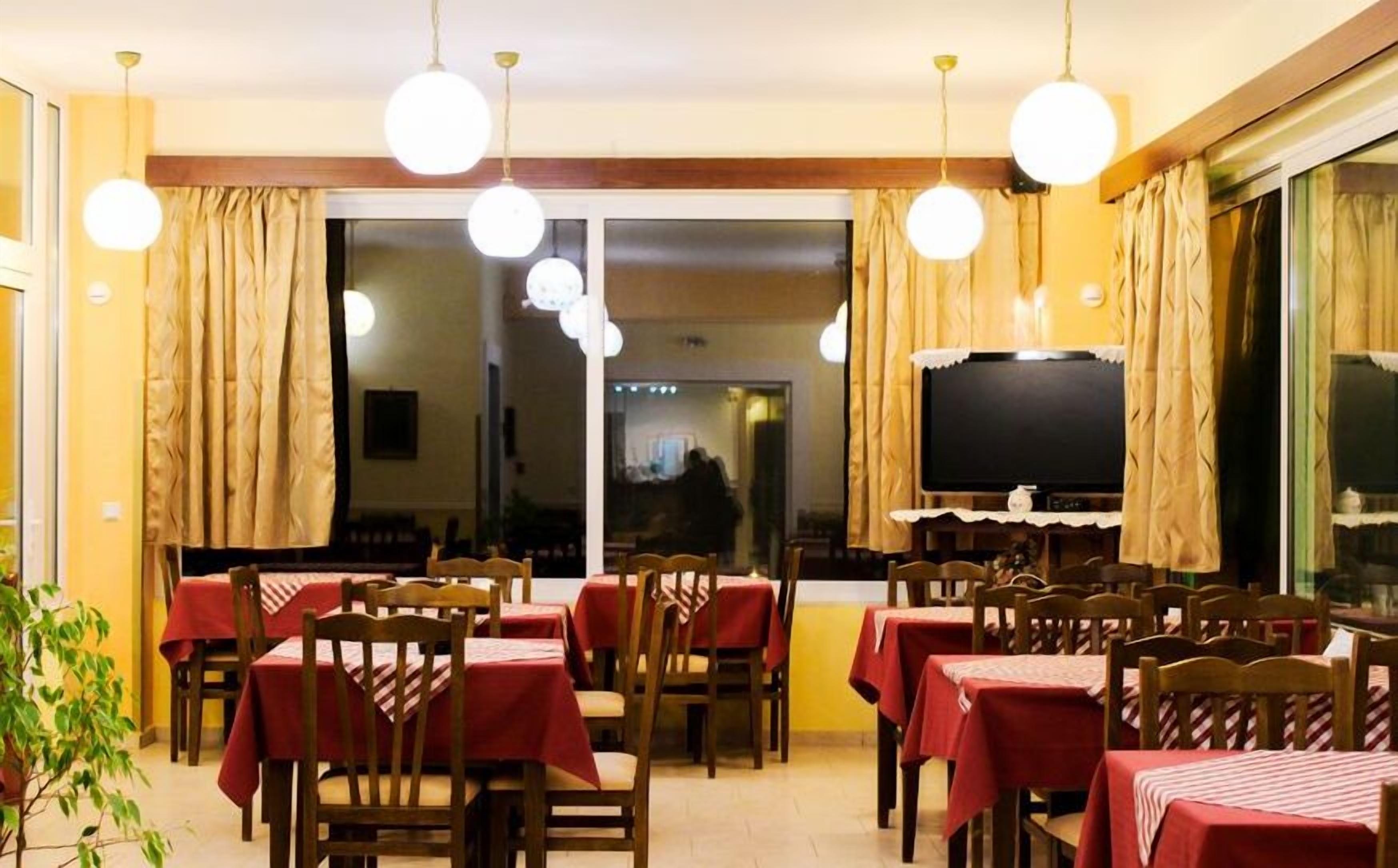 A restaurant with multiple tables and chairs, large windows with curtains, and hanging spherical light fixtures.