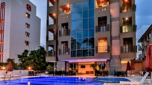 Un hotel moderno con zona de piscina, varios balcones y una entrada bien iluminada.