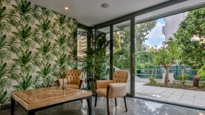 Un interior moderno con un amplio ventanal que da a un espacio exterior, que incluye un sofá mullido, una mesa de centro de madera y una pared con diseño.