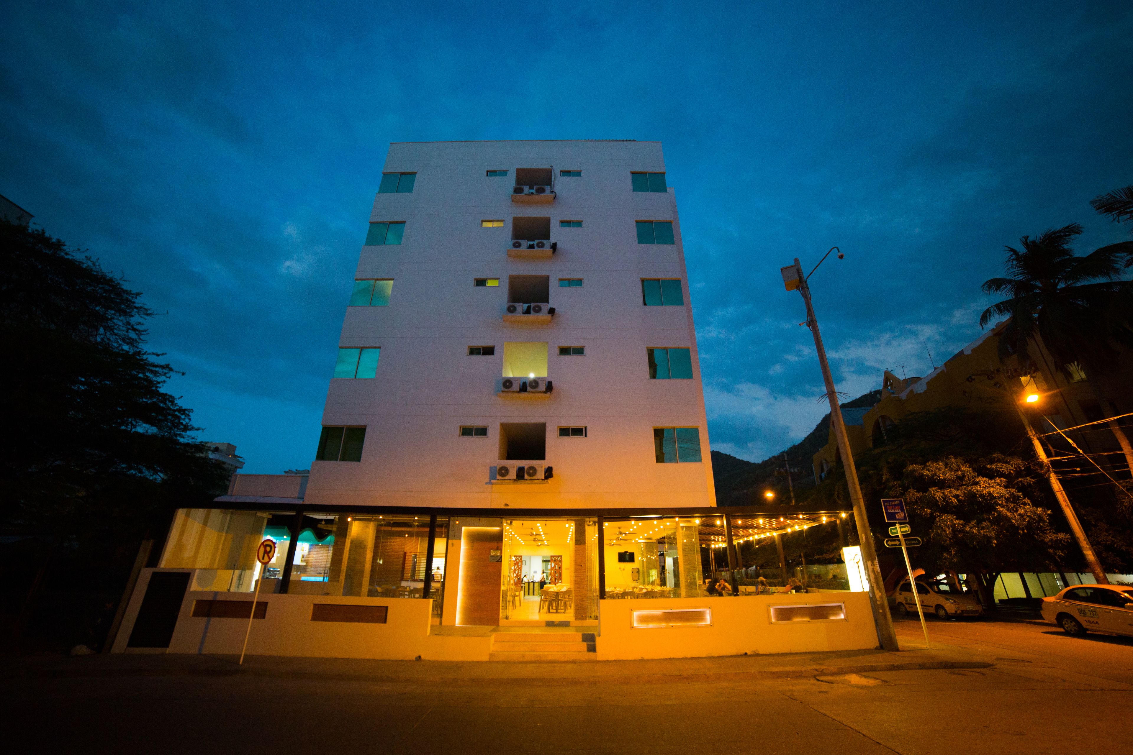 A multi-story hotel with a modern design, featuring a glass facade and a ground-level entrance with a seating area.