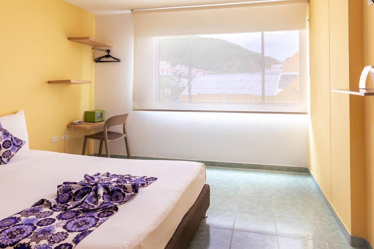 Un dormitorio con cama, escritorio, silla, ventana y vista al exterior.
