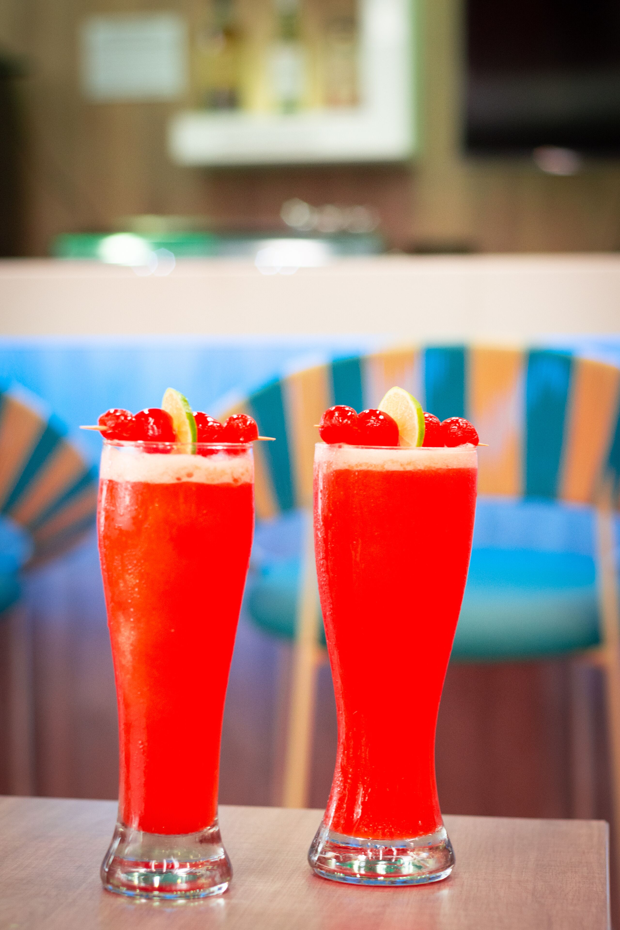 Two tall glasses of red beverage with garnishes, placed on a wooden table.