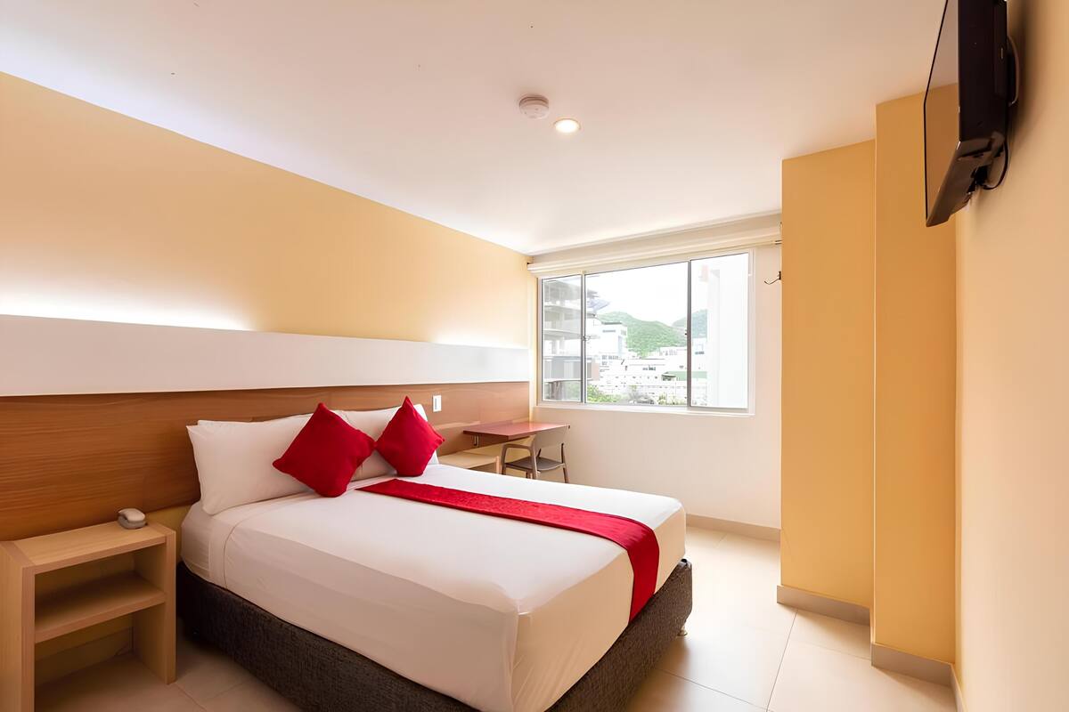 Una habitación de hotel con cama, mesita de noche y televisor montado en la pared.