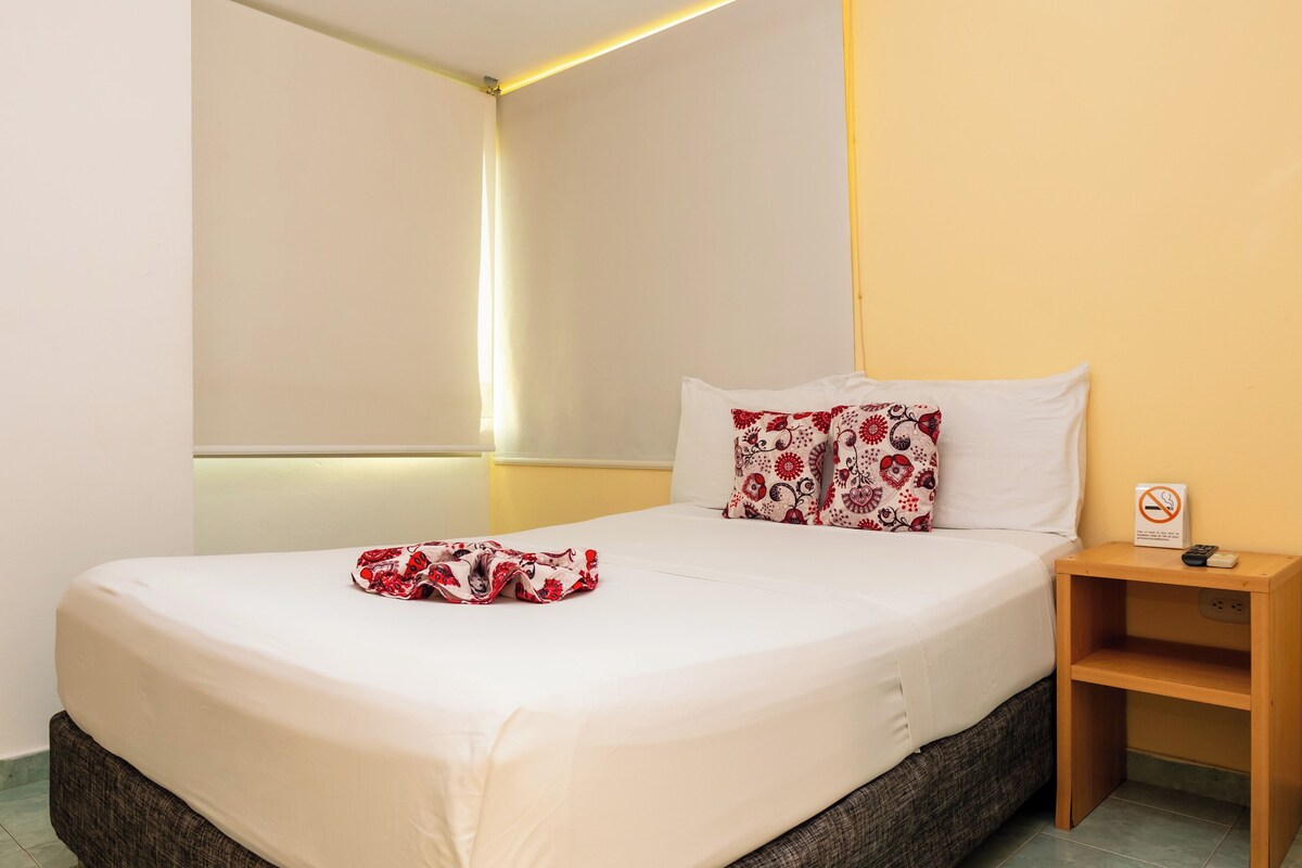 A hotel room with a bed, a bedside table, and a nightstand.