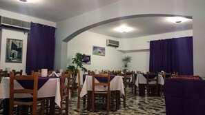 A dining area with tables and chairs, purple curtains, and a tiled floor. - Ogliastra Hotel (Lotzorai)