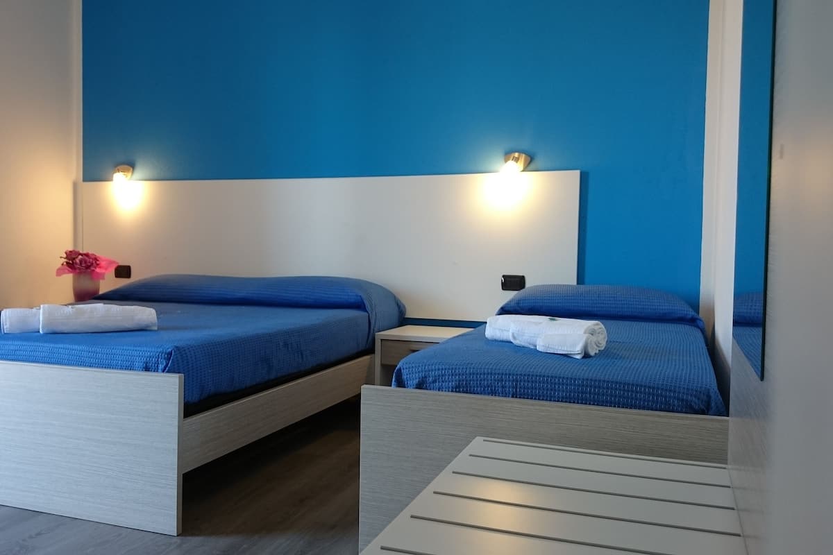 Une chambre d’hôtel avec deux lits, chacun doté d’un matelas bleu et d’une tête de lit blanche. Deux lampes murales sont fixées au-dessus de chaque lit.