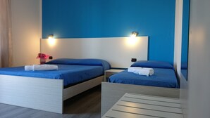 Habitación de hotel con dos camas, cada una con colchón azul y cabecero blanco. Dos luces empotradas en la pared sobre cada cama.