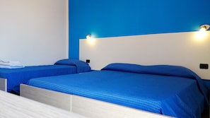 Two single beds with blue bedding in a room with a blue accent wall and two wall-mounted lights. - Ogliastra Hotel (Lotzorai)