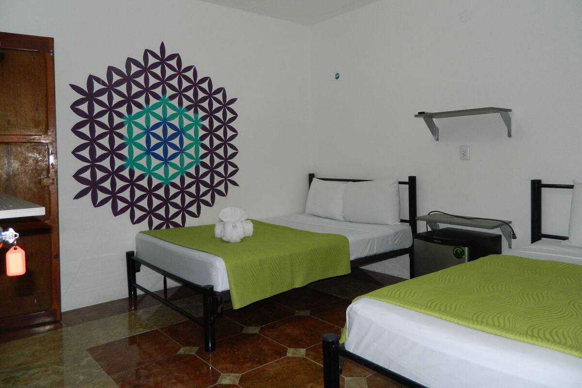 A hotel room with two beds, a decorative geometric wall art, a wooden door, and a tiled floor.