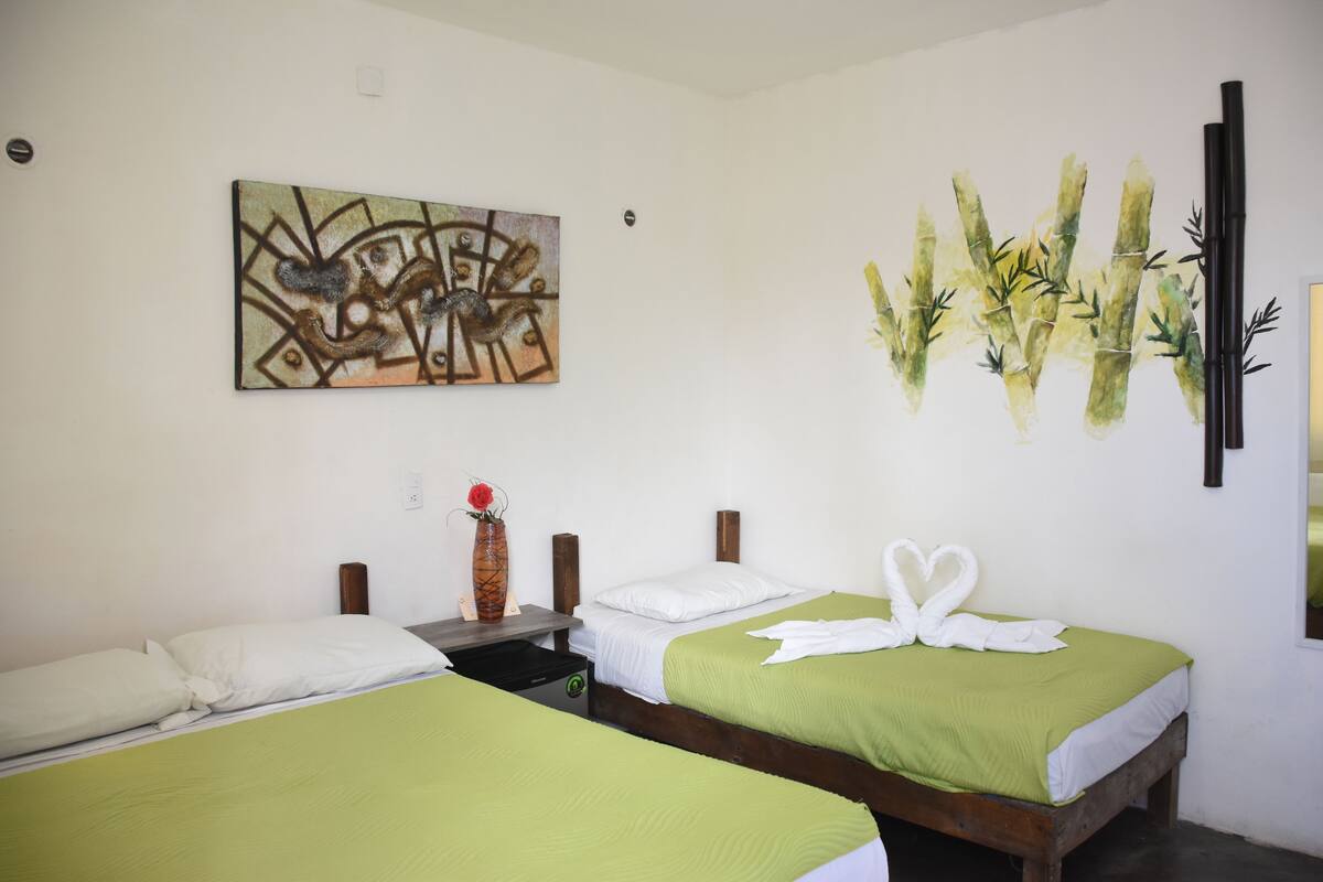 A hotel room with two beds, a painting, and a bamboo wall decoration.