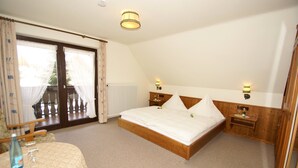 A bedroom with a wooden bed, two bedside tables, a nightstand, a window with curtains, and a view of the outside. - Hotel-Restaurant SchöpPerle (Häusern)