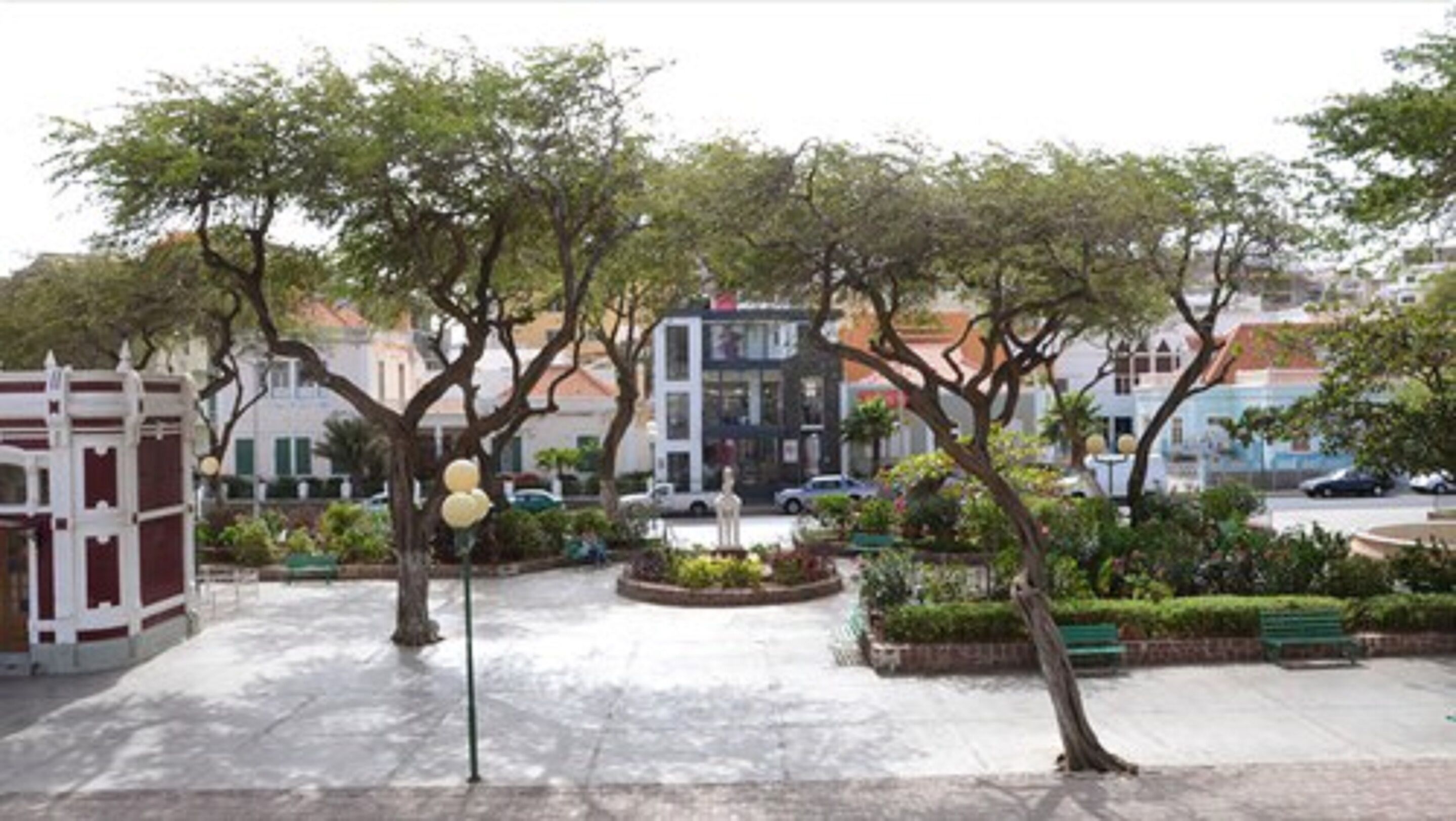 A public square with trees, benches, and a statue.