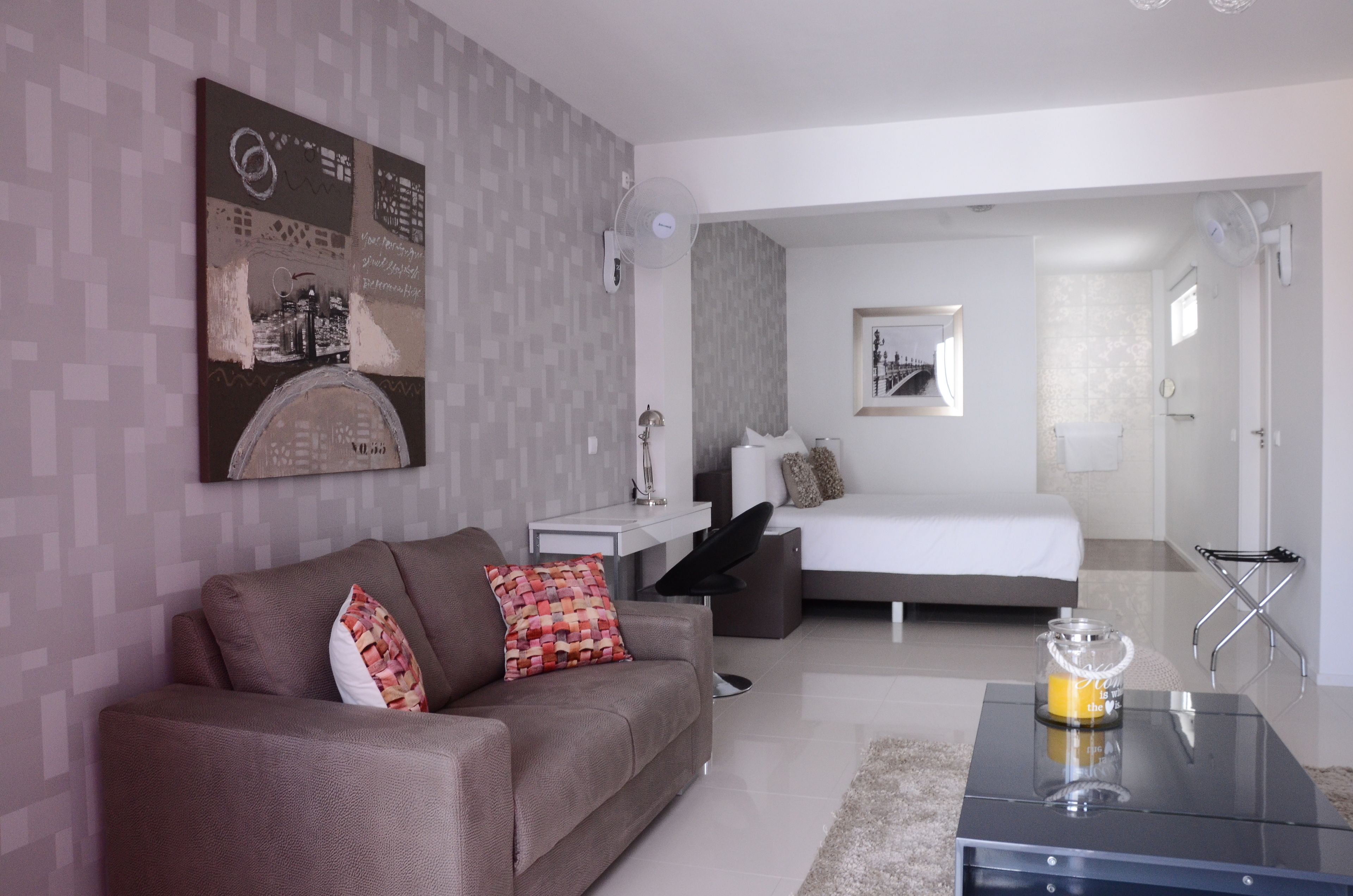 A modern hotel room with a sofa, a bed, a bedside table, and a glass coffee table.