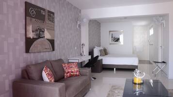 A modern hotel room with a sofa, a bed, a bedside table, and a glass coffee table.