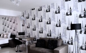 Ein modernes Schlafzimmer mit Bett, Schreibtisch und einer Couch. Die Wände sind mit einem Muster der Eiffelturms verziert.