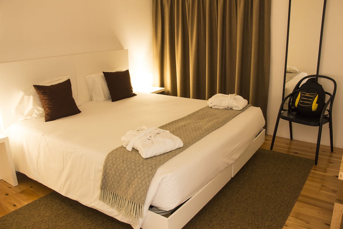 Un lit bien fait, avec des draps blancs, un plaid marron et une serviette pliée posée sur le côté.
