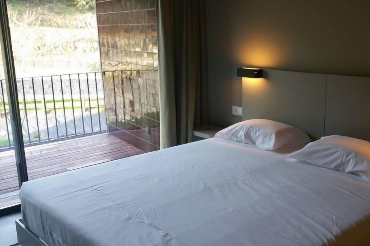 Une chambre d’hôtel avec un grand lit, deux lampes de chevet et une vue sur un balcon.