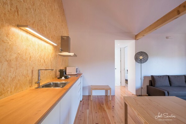 A modern kitchen with a wooden countertop, stainless steel sink, and a microwave. There is a small wooden table and a floor lamp in the room.