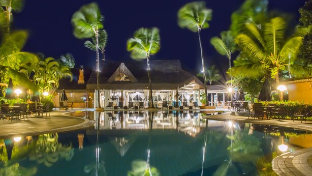 A nighttime resort pool area with palm trees, a thatched-roof building, and outdoor seating. - Mar Paraíso Hotel (Porto Seguro)