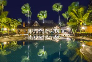 A nighttime resort pool area with palm trees, a thatched-roof building, and outdoor seating. - Mar Paraíso Hotel (Porto Seguro)