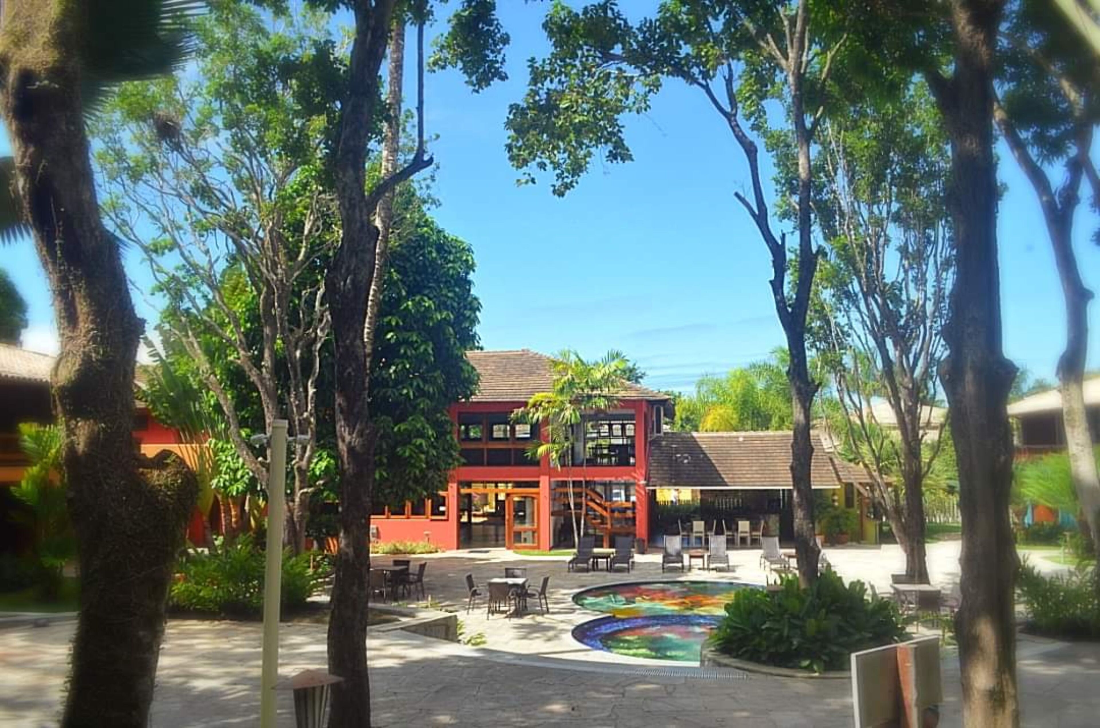 Un patio con piscina, mobiliario exterior y un edificio de varios pisos con grandes ventanales.