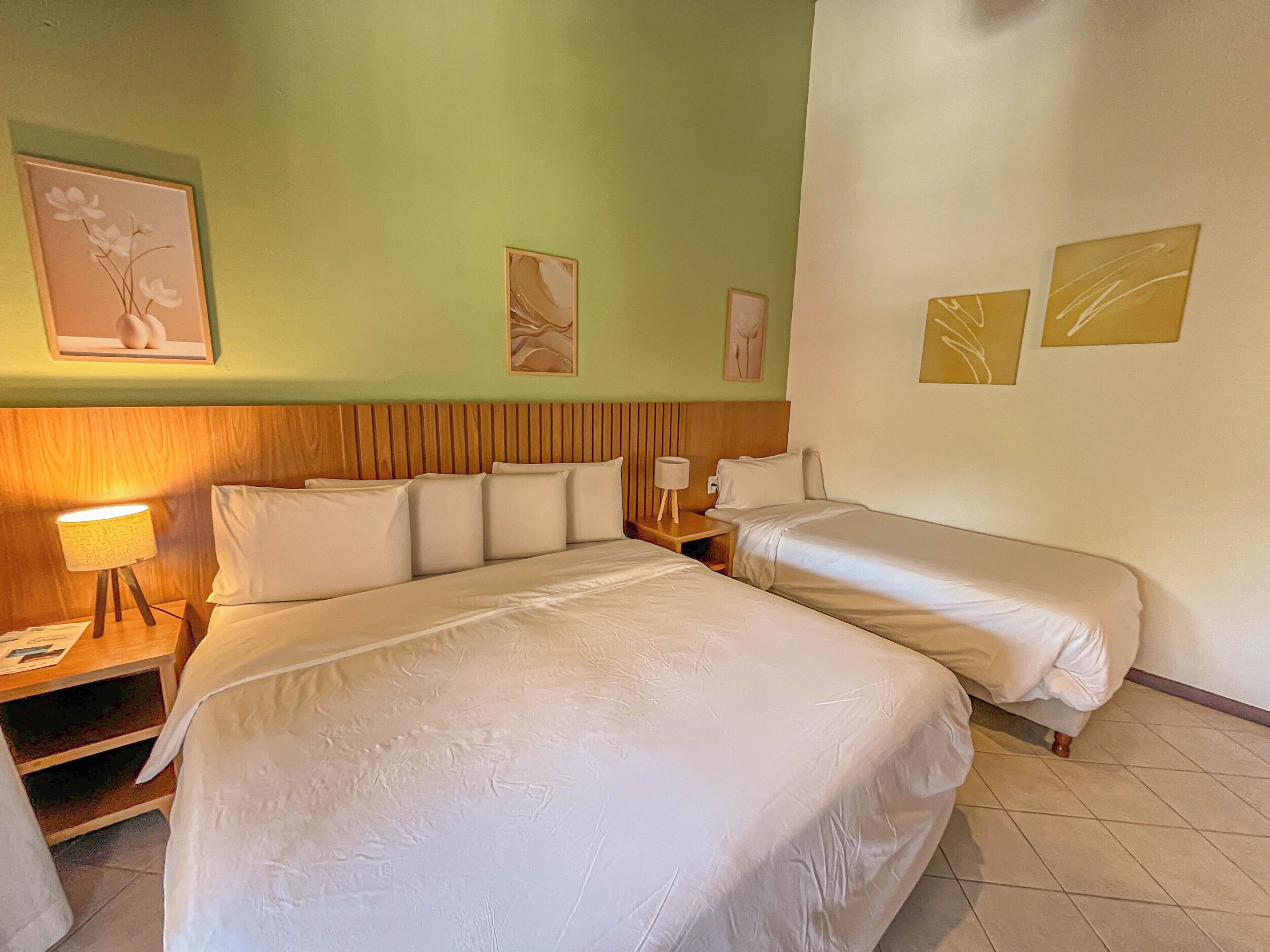 Una habitación de hotel con una cama grande, dos mesitas de noche, una lámpara y obras de arte en las paredes.