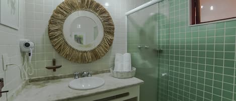 A bathroom with a round mirror, white sink, and green tiled walls.