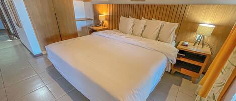 A hotel room with a large bed, wooden headboard, bedside tables with lamps, and a framed picture on the wall.