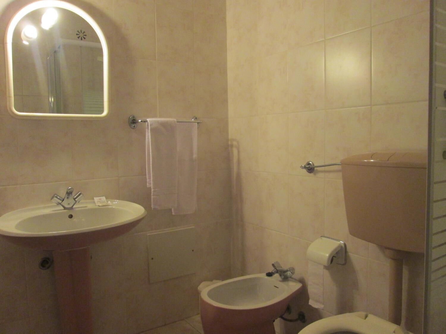 A bathroom with a sink, bidet, toilet, and a mirror with lights.
