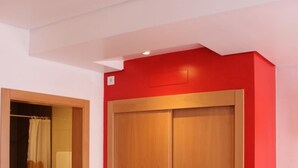 A room with a wooden wardrobe, a red wall, and a shower area. - Alojamento Baleal à Vista (Peniche)