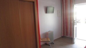 A room with a wooden wardrobe, a radiator, a television on the wall, and a chair. - Alojamento Baleal à Vista (Peniche)