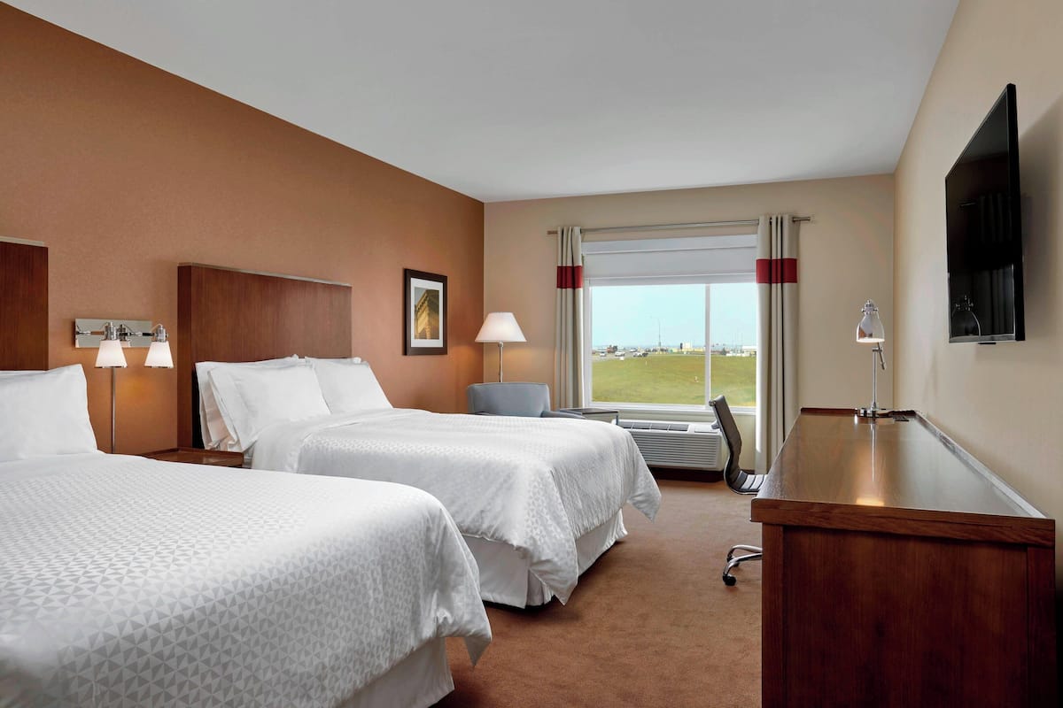 A hotel room with two beds, a desk, a chair, a TV, and a window with a view.