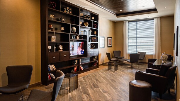 A modern lounge area with a large entertainment unit, comfortable seating, and a large window providing natural light. - Four Points By Sheraton Sherwood Park (Sherwood Park)