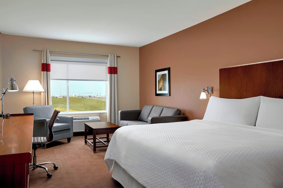 A hotel room with a large bed, two armchairs, a desk, and a window with curtains.