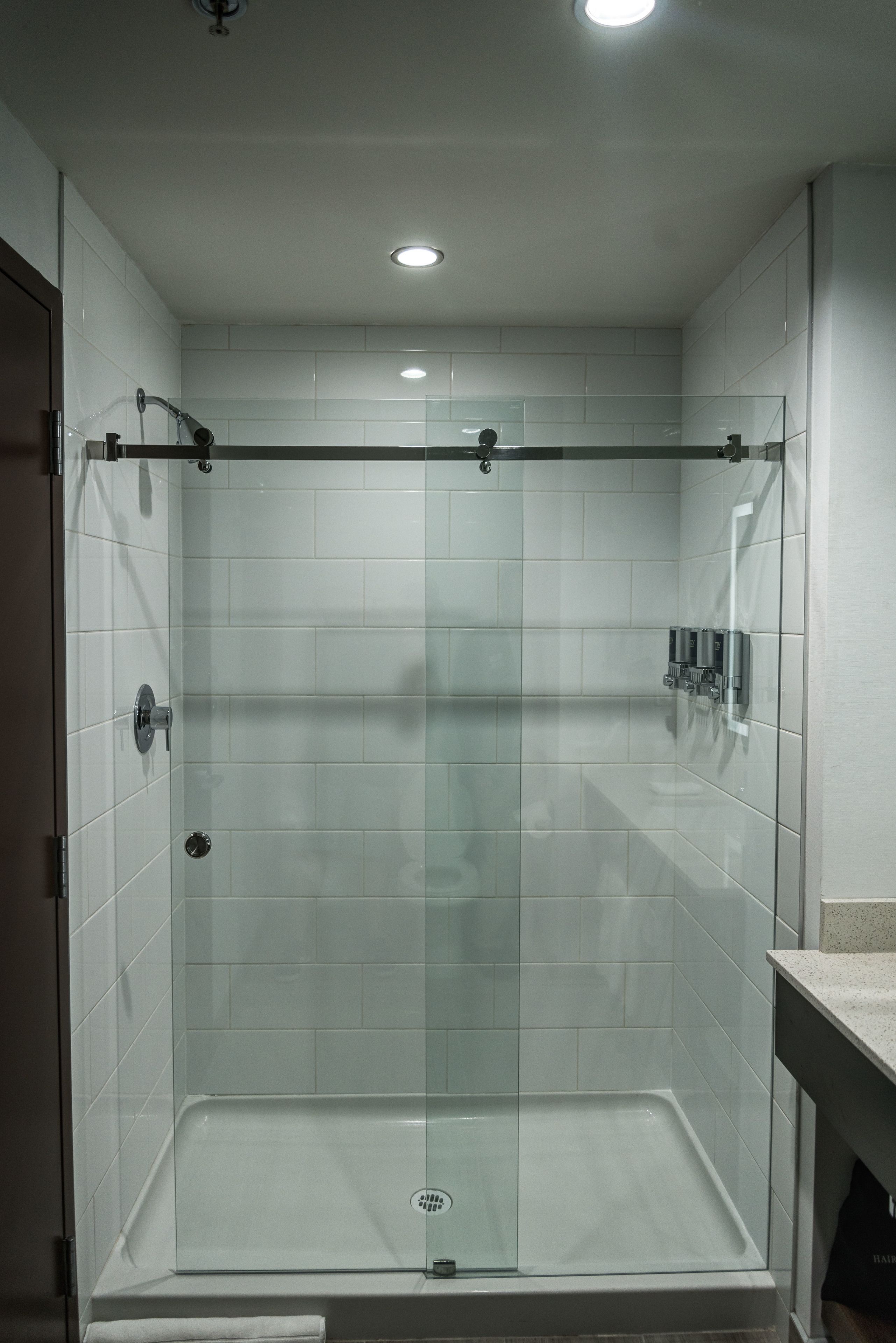 A glass-enclosed shower with a control panel on the wall, a glass door, and a tiled floor.