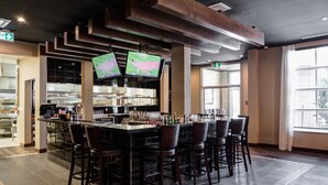A bar area with multiple screens, bar stools, and a kitchen in the background. - Four Points By Sheraton Sherwood Park (Sherwood Park)