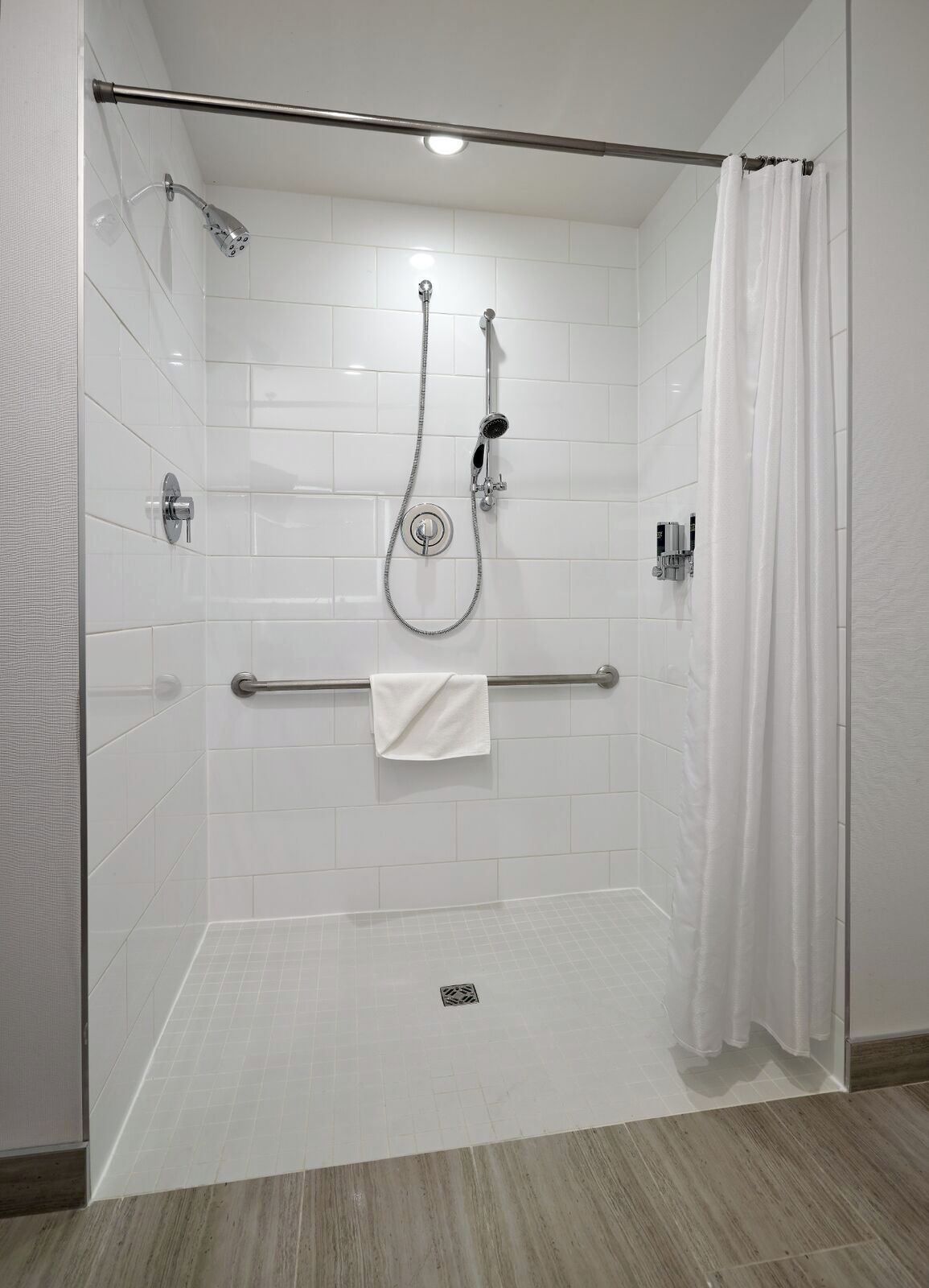 Ducha a ras de suelo con paredes de azulejos blancos, puerta de cristal y cabezal de ducha.