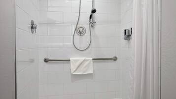 Ducha a ras de suelo con paredes de azulejos blancos, puerta de cristal y cabezal de ducha.