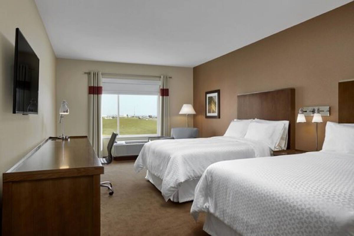 A hotel room with two beds, a desk, a chair, a window with curtains, and a painting on the wall.