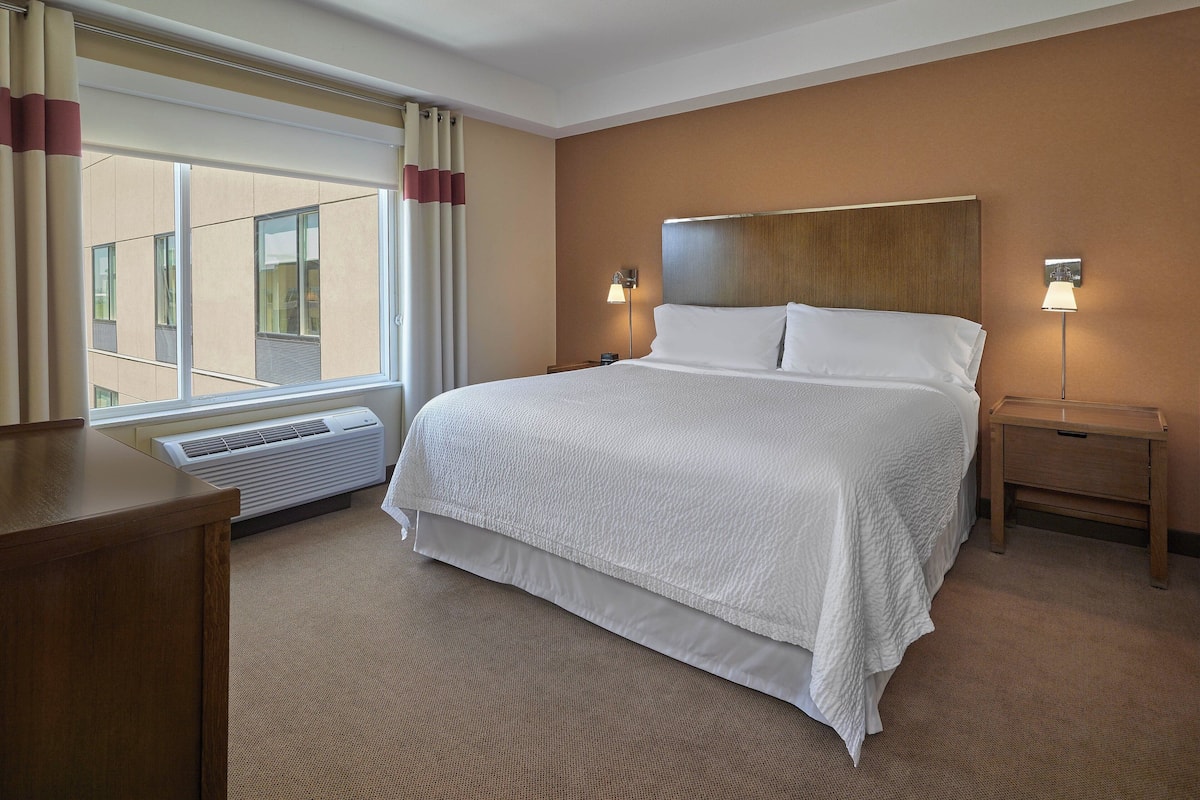 A hotel room with a large bed, a bedside table, a lamp, and a window with curtains.