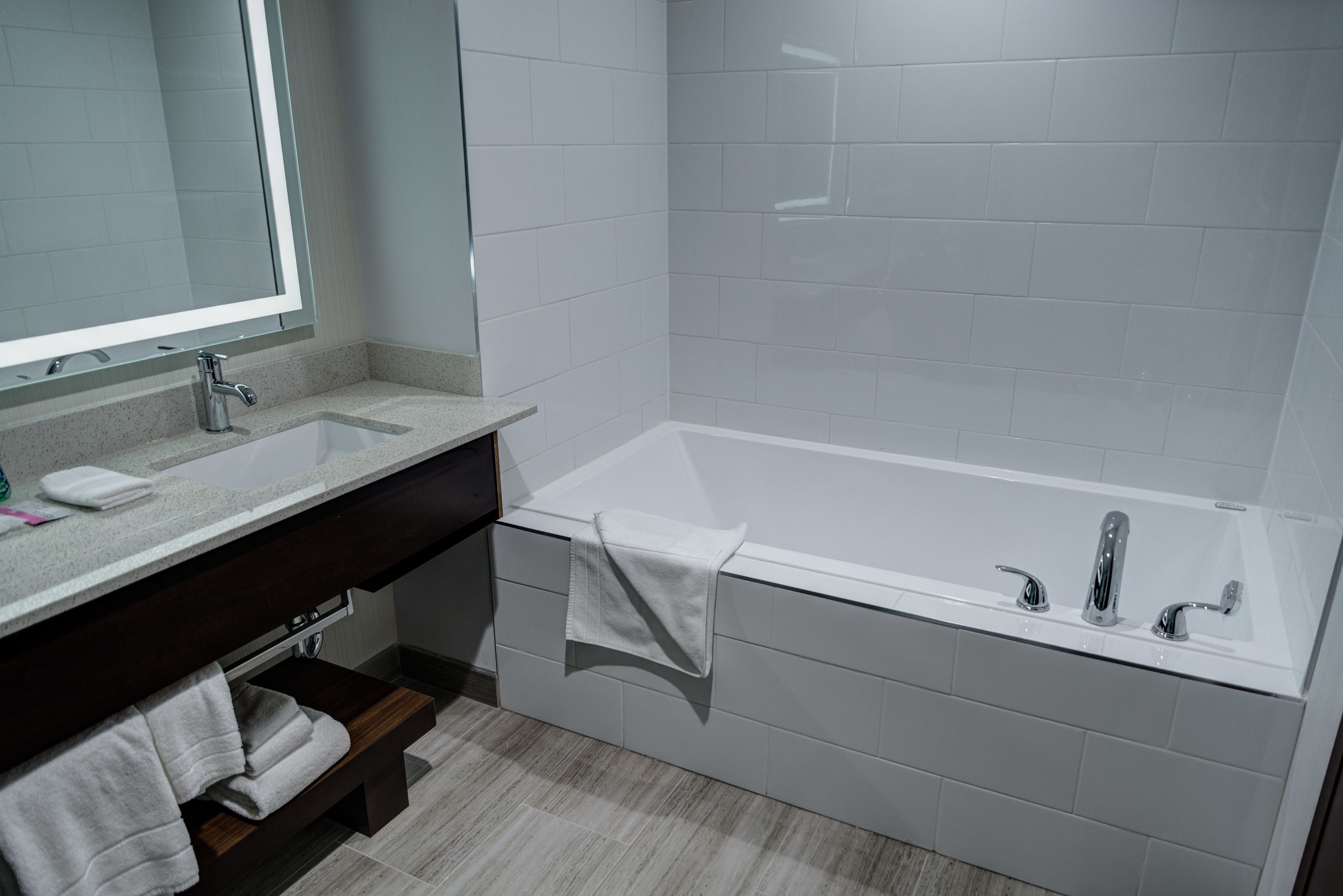 A modern bathroom with a white bathtub, a large mirror, and a dark wooden vanity.