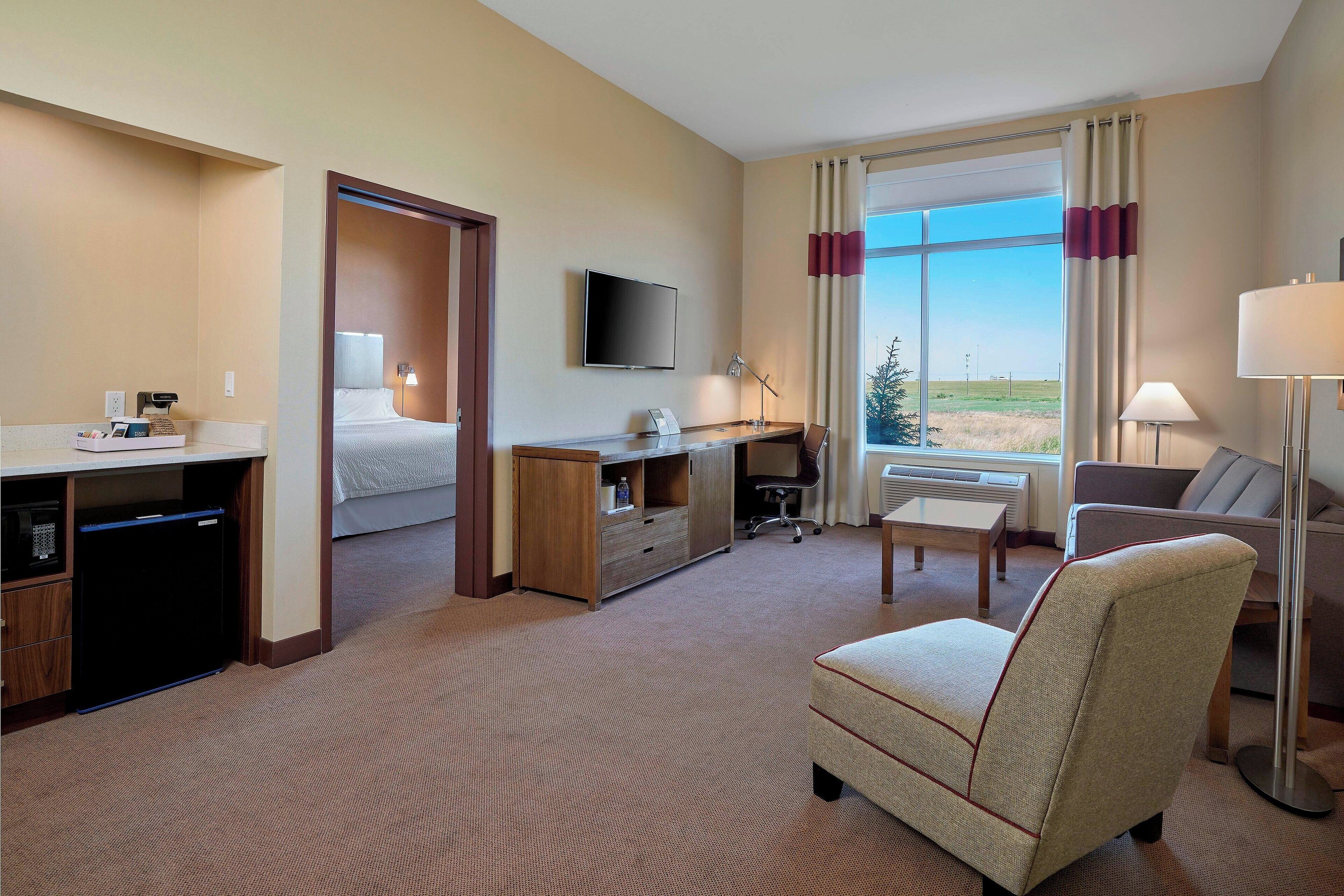A hotel room with a bed, desk, chair, TV, and large window with curtains.