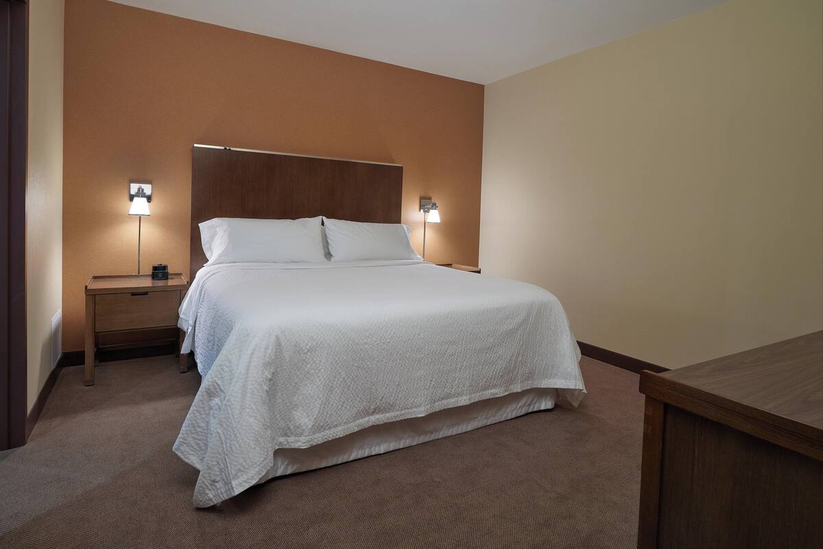 A neatly made bed with white linens, two bedside lamps, and a wooden headboard in a hotel room.