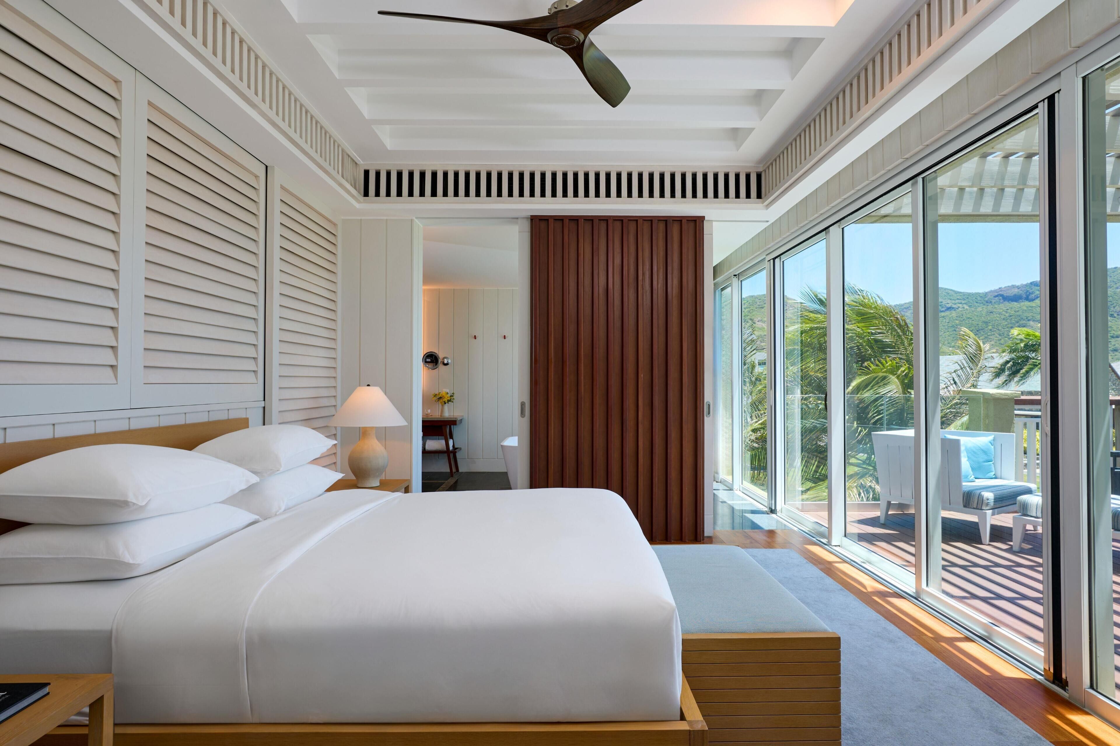 A modern hotel room with a large bed, a ceiling fan, a view of the outdoors, and a wooden wall.