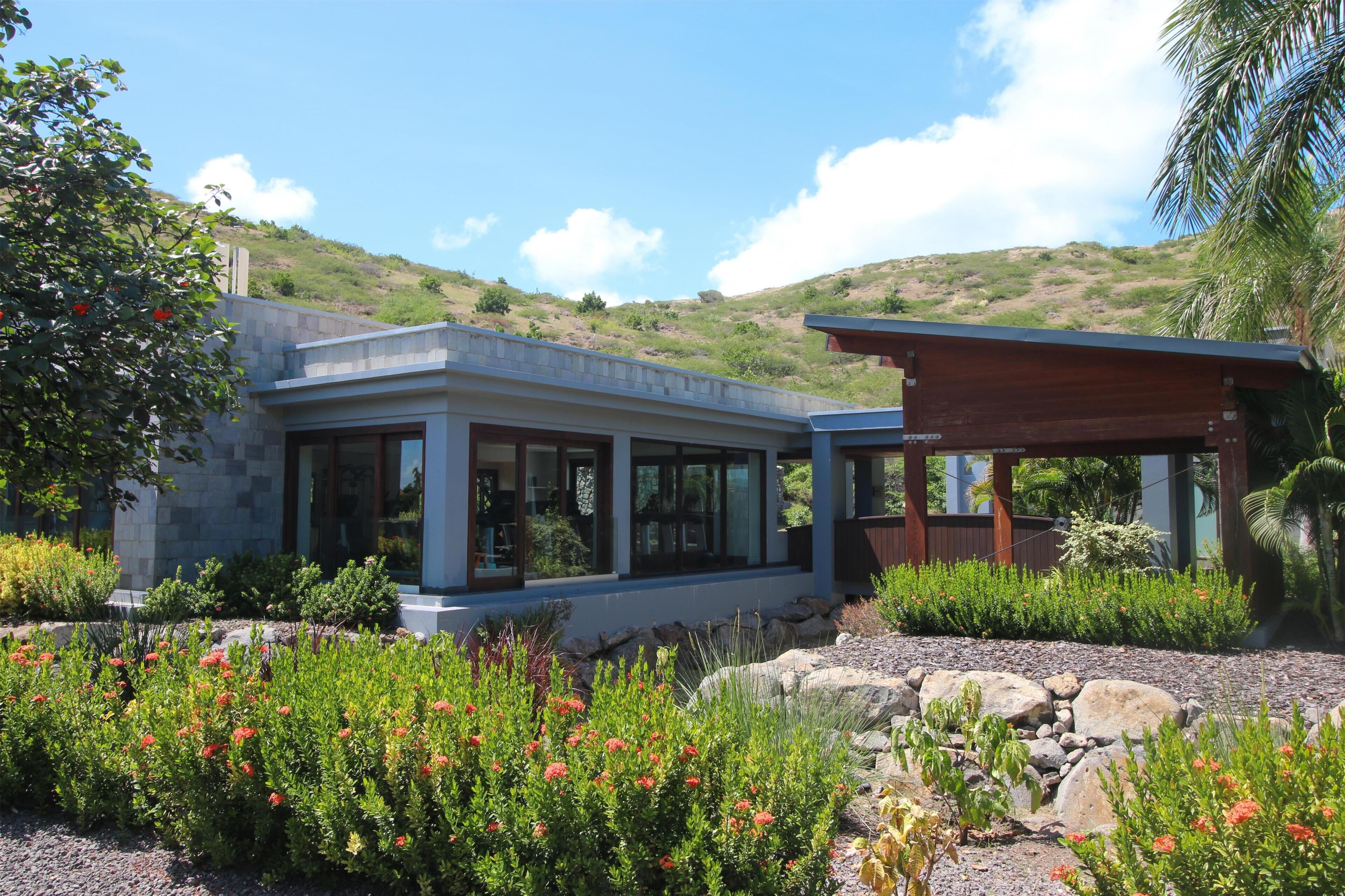 A modern house with a stone facade, large windows, and a garden with red flowers.