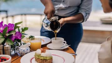 A breakfast setting with a person pouring coffee into a cup, a plate with a pastry, and a fruit bowl.