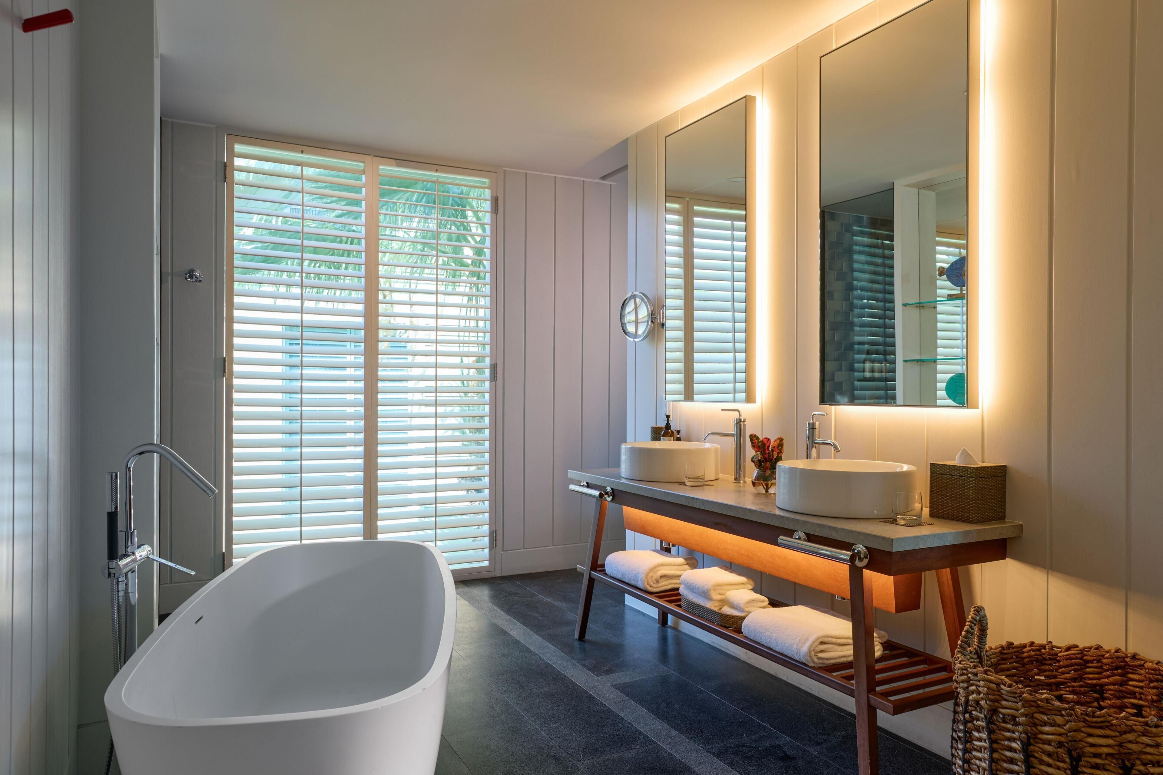 Un baño moderno con una bañera independiente, un tocador con espejo y una ventana con persianas.
